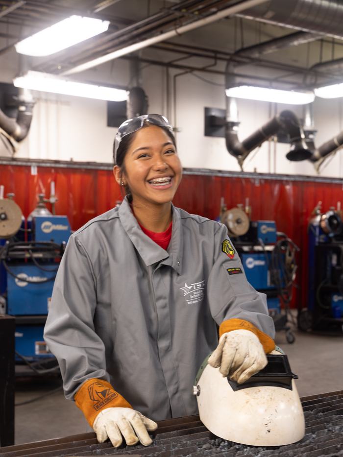 A young woman in welding gear in a technical college welding lab