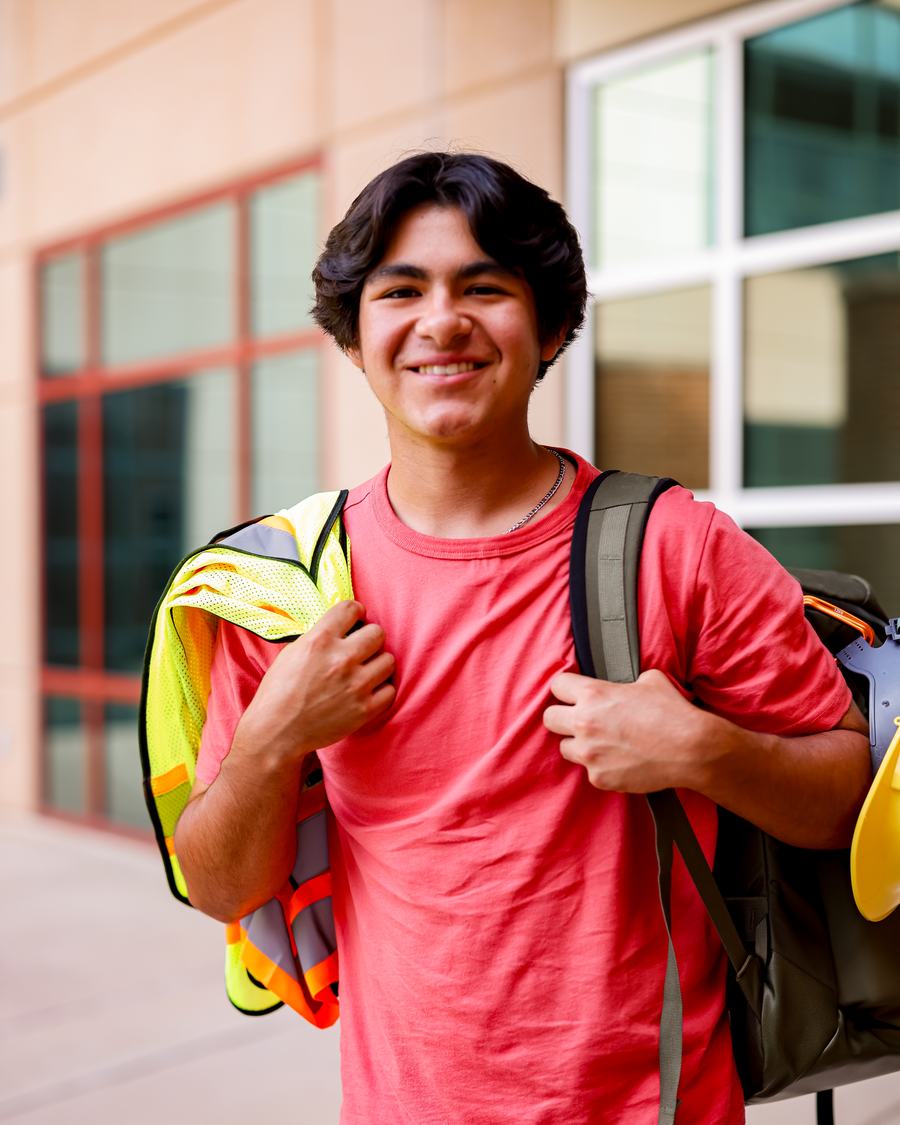A West Texas high school student carrying a hard hat, safety vest and backpack outside his campus